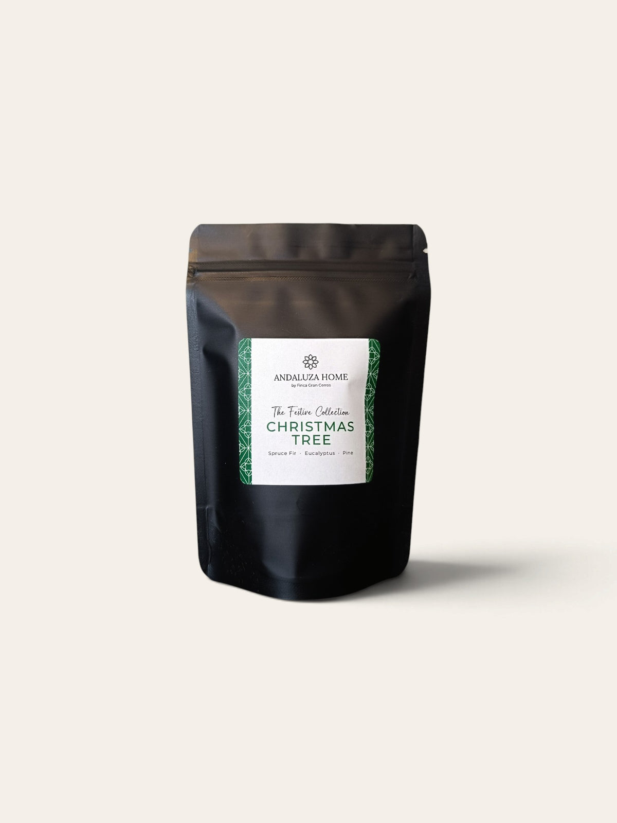 A matte black stand-up pouch with a white and green label reading 'Christmas Tree Fragrance Oil - The Festive Collection' by Andalusia Home, centered on a light warm-gray background.
